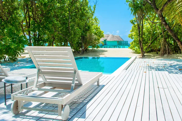 Lhaviyani Atoll, Maldives - 13 Temmuz 2018: havuzda şezlong ve şemsiyeler palmiye ağaçları gölgesinde ile Hint Okyanusu kıyısında alanı