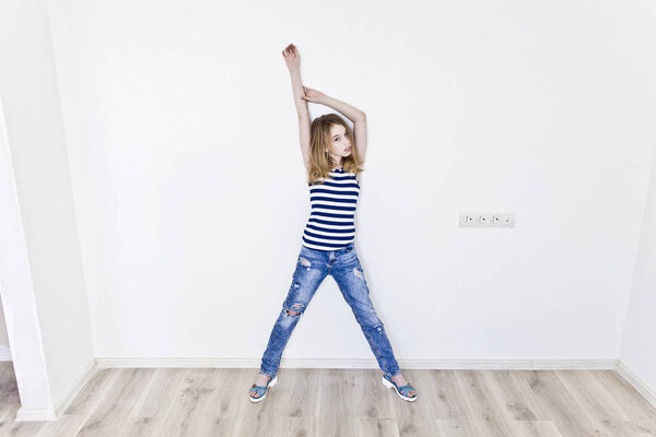 Girl eleven years old with blond hair standing near white wall and upwards hands