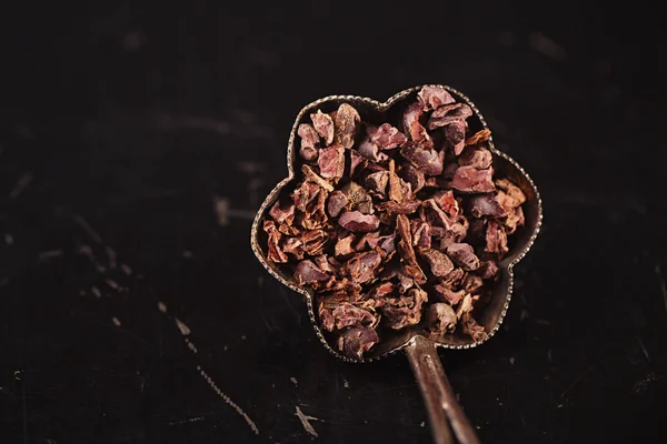 raw cacao nibs in vintage silver bowl on dark metal background