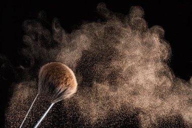 Siyah bir arka plan üzerinde toz uçan ile makyaj için fırça izole.