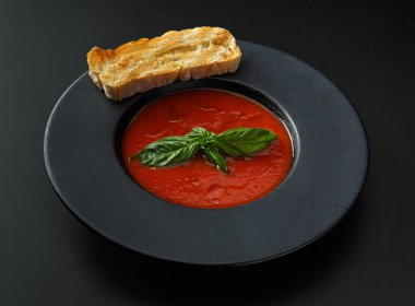 bir tost ve fesleğen izole bir siyah arka plan üzerine siyah bir plaka ile domates çorbası.