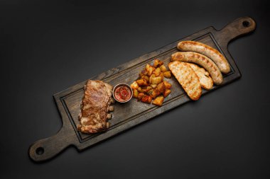 Sosis ile Yönetim Kurulu; Pirzola, patates ve sosu bir siyah arka plan üzerine izole bira için.