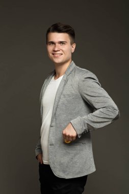 Bir ceketi giyen genç bir adam bir sikke bitcoin cebinde bir gri arka plan üzerine koyar.