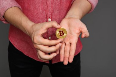 kırmızı gömlekli bir genç adam ve onun elinde, gri bir arka plan üzerinde izole bir bitcoin para portre.