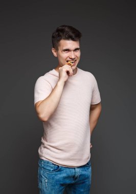 Genç adam bir sikke bitcoin dişleriyle, özgünlük, gri bir arka plan üzerinde izole denetleme ısırıkları.