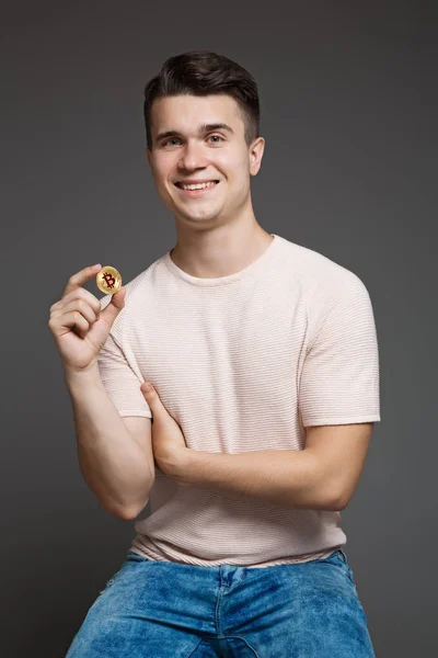 若い男の手でコイン Bitcoin を保持して 笑みを浮かべて 灰色の背景に分離 — ストック写真