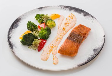 Bir parça kızarmış somon balık beyaz arka plan üzerinde izole bir tabakta sebze ve sos ile.