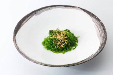Beyaz arka plan üzerinde izole bir beyaz tabak susam serpilir yeşil yosun salata.