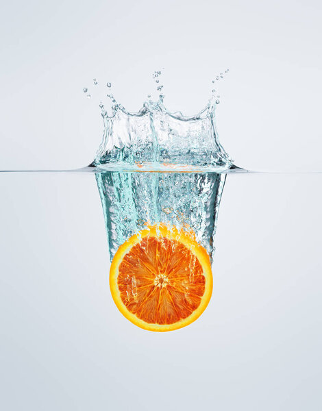 a slice of red orange falls into the water discarding a lot of s