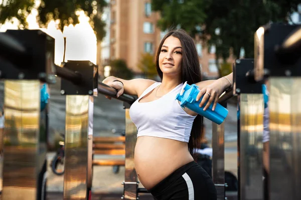 Incinta, ragazza atletica nel parco giochi con uno shaker in mano — Foto Stock