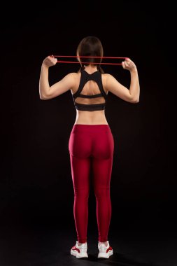 Siyah arka planda izole edilmiş kauçuk genişleticiyle egzersiz yapan genç, zayıf bir kız..