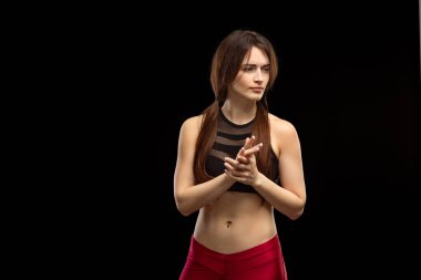 Genç, zayıf bir kız, antrenör, siyah arka planda izole edilmiş jestler gösteriyor.