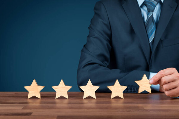 Increase rating, evaluation and classification concept. Businessman sitting behind a table and add fifth wooden star.