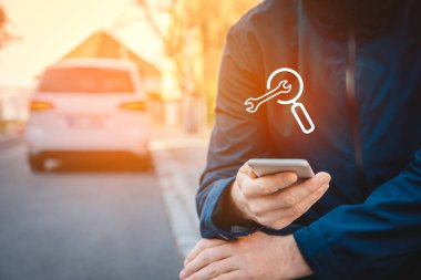 Akıllı telefondan araba servisini ara. Akıllı araba ve araba konseptinde yeni teknolojiler. Elinde akıllı telefon olan biri kaldırımda oturuyor ve en yakın servisi arıyor..