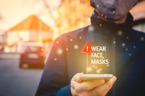 戴口罩推荐 有智能手机的人走在街上 在大流行的时候看手机上戴口罩的告示 — 图库照片