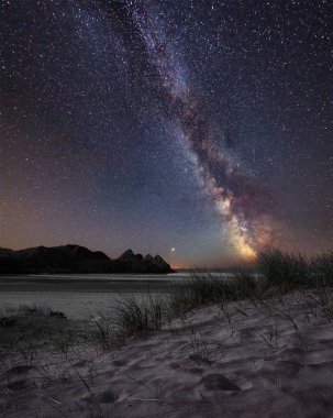 Stunning vibrant Milky Way composite image over landscape of yellow sandy beach Three Cliffs bay clipart