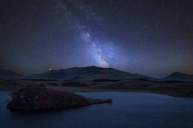 Stunning vibrant Milky Way composite image over landscape of Llyn y Dywarchen lake in Snowdonia National Park clipart
