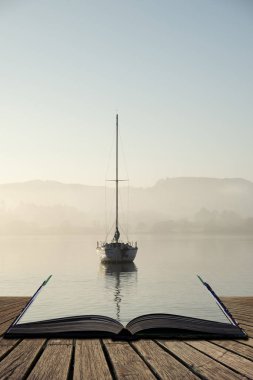 Beautiful unplugged landscape image of sailing yacht sitting still in calm lake water in Lake District during peaceful misty Autumn Fall sunrise coming out of pages of open story book clipart