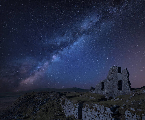Stunning vibrant Milky Way composite image over abandoned Foggintor Quarry in Dartmoor with raking soft sunlight over ruins and derelict buildings