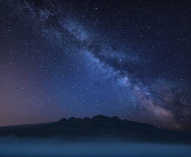 Stunning vibrant Milky Way composite landscape image over the tors in Dartmoor revealing peaks through the mist clipart