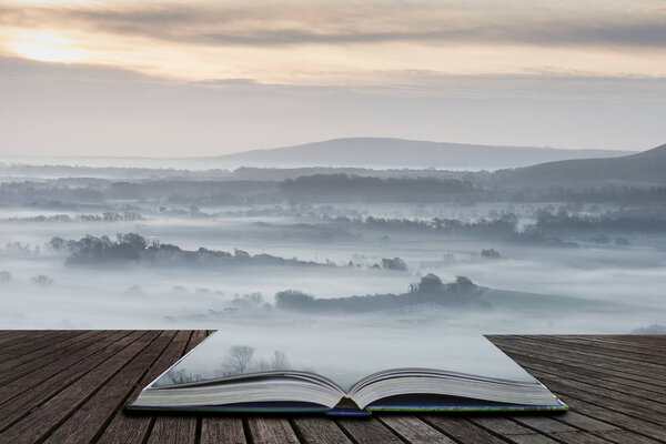 Beautiful foggy English countryside landscape at sunrise in Winter with layers rolling through the fields coming out of pages in magical story book
