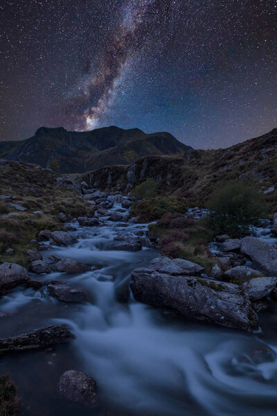 Stunning vibrant Milky Way composite image over Landscape image of river flowing down mountain range near Llyn Ogwen and Llyn Idwal in Snowdonia