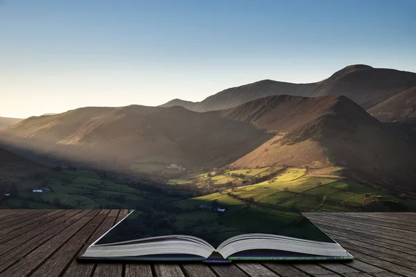 Stunning landscape image of sun beams lighting up small area of mountain side in Lake District coming out of pages of open story book