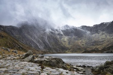 Beautiful moody Winter landscape image of Llyn Idwal and snowcap clipart