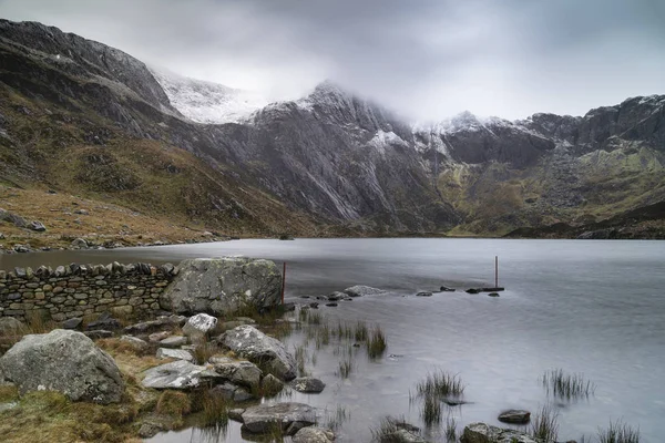 Piękny nastrojowy zimowy krajobraz wizerunek Llyn Idwal i Snowcap — Zdjęcie stockowe