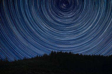 Snowdonia 'daki Çam ağacı sırtı manzaralı Polaris etrafındaki yıldız izlerinin dijital bileşik görüntüsü.