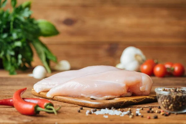 Raw chicken fillets on a cutting board against the background of a wooden table. Concept of cooking.