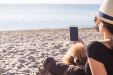 Kadın gezgin tutuyor smartphone, süre açık havada deniz üzerinde yaptığı yolculuk sırasında rahatlatıcı. Kadın köpeğiyle seyahat.