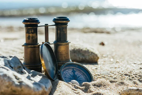 Old vintage compass and binoculars on the sand beach. Travel navigation concept .