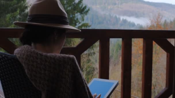 女性旅行者は 旅行中に美しい山の風景に対してタブレットでテラスに座っています フリーランスまたはリモートのビジネス ブロガー ライターの概念 — ストック動画