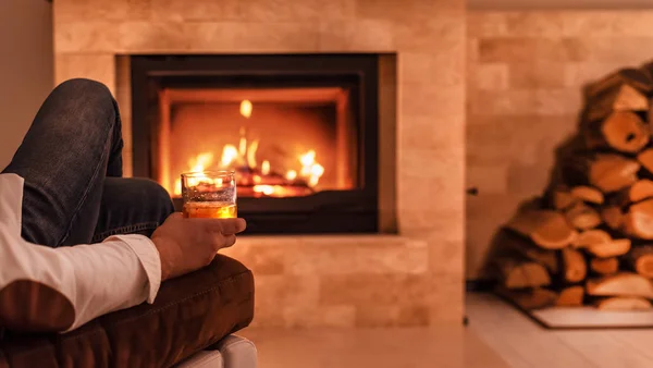 Man sitting at home by the fireplace and drinking a whiskey.