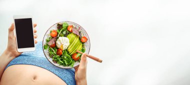 Genç kadın bir salata yemek ve bir fitness app bir egzersiz yaptıktan sonra onun smartphone kullanarak.