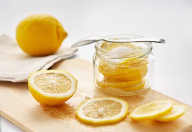 Dilimler limon şeker ile serpilir, cam kavanozun içinde olur. Yakın, ahşap kesme tahtası üzerinde dilimlenmiş limon olduğunu.