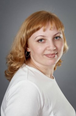 Genç bir kadın gülümseyerek ve kameraya bakıyor. Gri arka planı