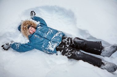 Bir çocuk sıcak giysiler içinde kar üzerinde gülümseyen ve kameraya bakarak yalan söylüyor.