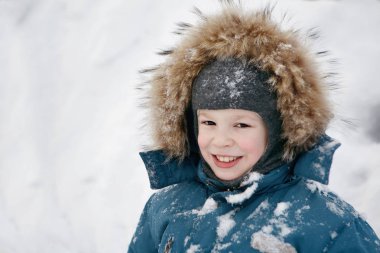 Sıcak giysiler içinde bir oğlan kameraya bakarak ve gülümseyen. 