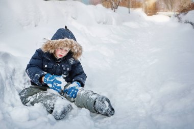 Çocuk karlı bir yol üzerinde oturur ve kartopu oynuyor