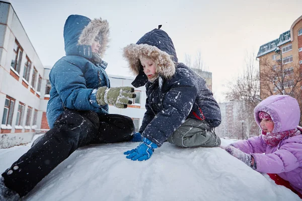 Three children playing on a snow hill. Snowing.