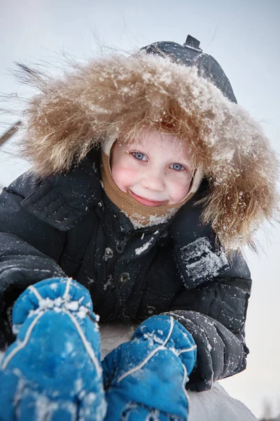 一个穿着暖和衣服的男孩躺在雪地上 微笑着看着镜头 — 图库照片