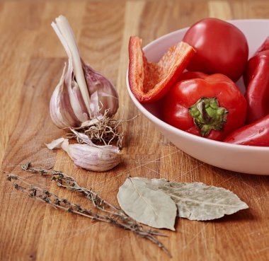 Ahşap masaya sarımsak, defne yaprağı ve dal fesleğen olduğunu. Pembe bir kase biber ile yakın olduğunu.