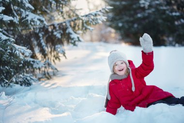 küçük kız kırmızı paltolu karda oturan ve gülümseyen.