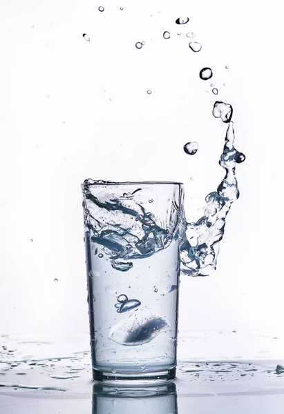 Spruzzi d'acqua in un bicchiere di vetro. Fondo bianco . — Foto Stock