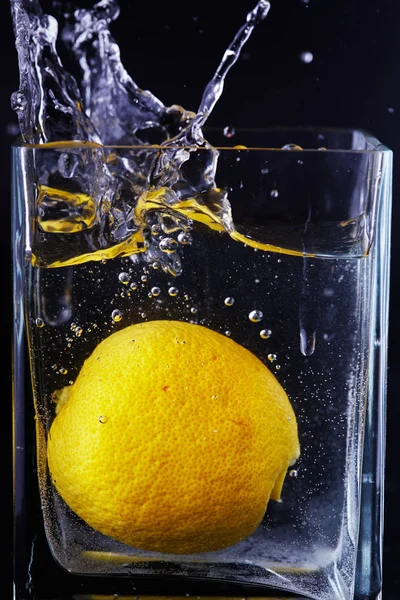 Lemon est tombé dans un bocal en verre avec de l'eau. Fond noir . — Photo