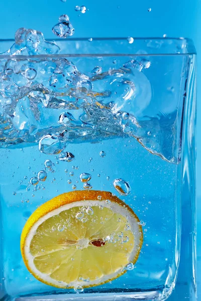 Un pezzo di limone in un vaso di vetro. Fondo blu . — Foto Stock