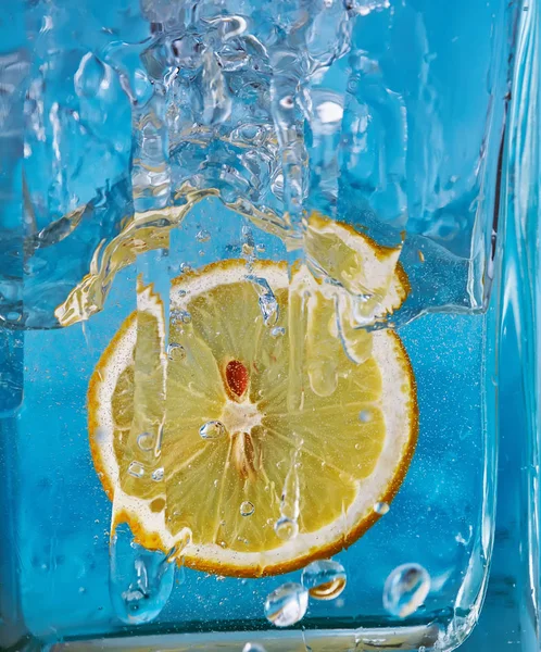 Un trozo de limón en un recipiente de vidrio. Fondo azul . —  Fotos de Stock