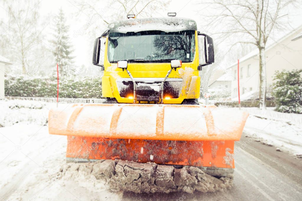 Snowplow removes snow off icy road in winter